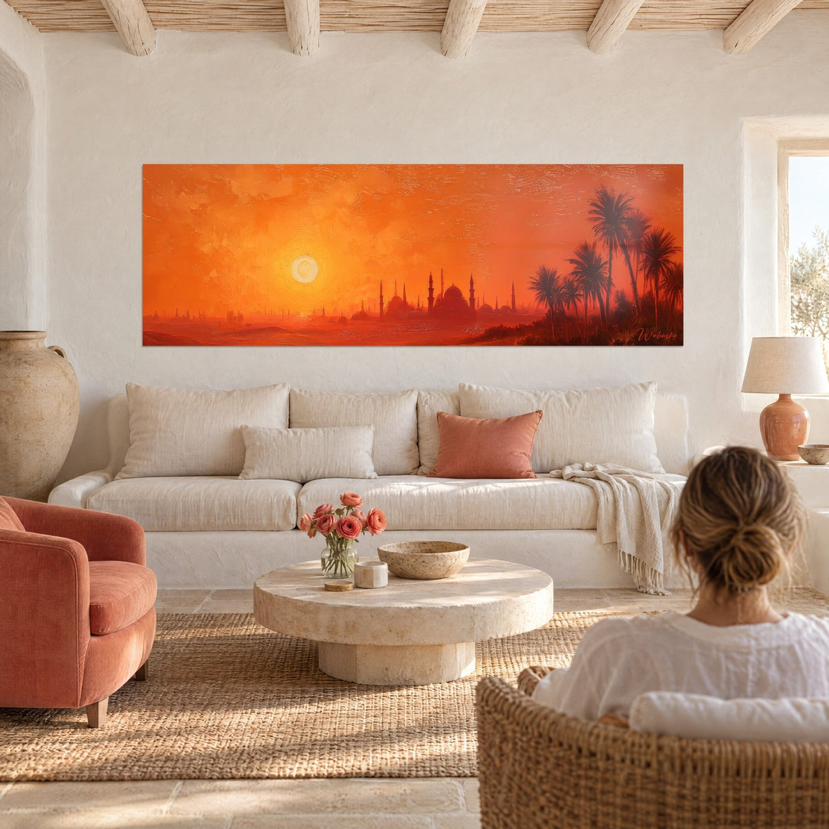 Tableau coucher de soleil orange sur mosquée et minarets, palmiers ombrés à droite, vu par une femme de dos au-dessus d'un canapé dans un salon lumineux