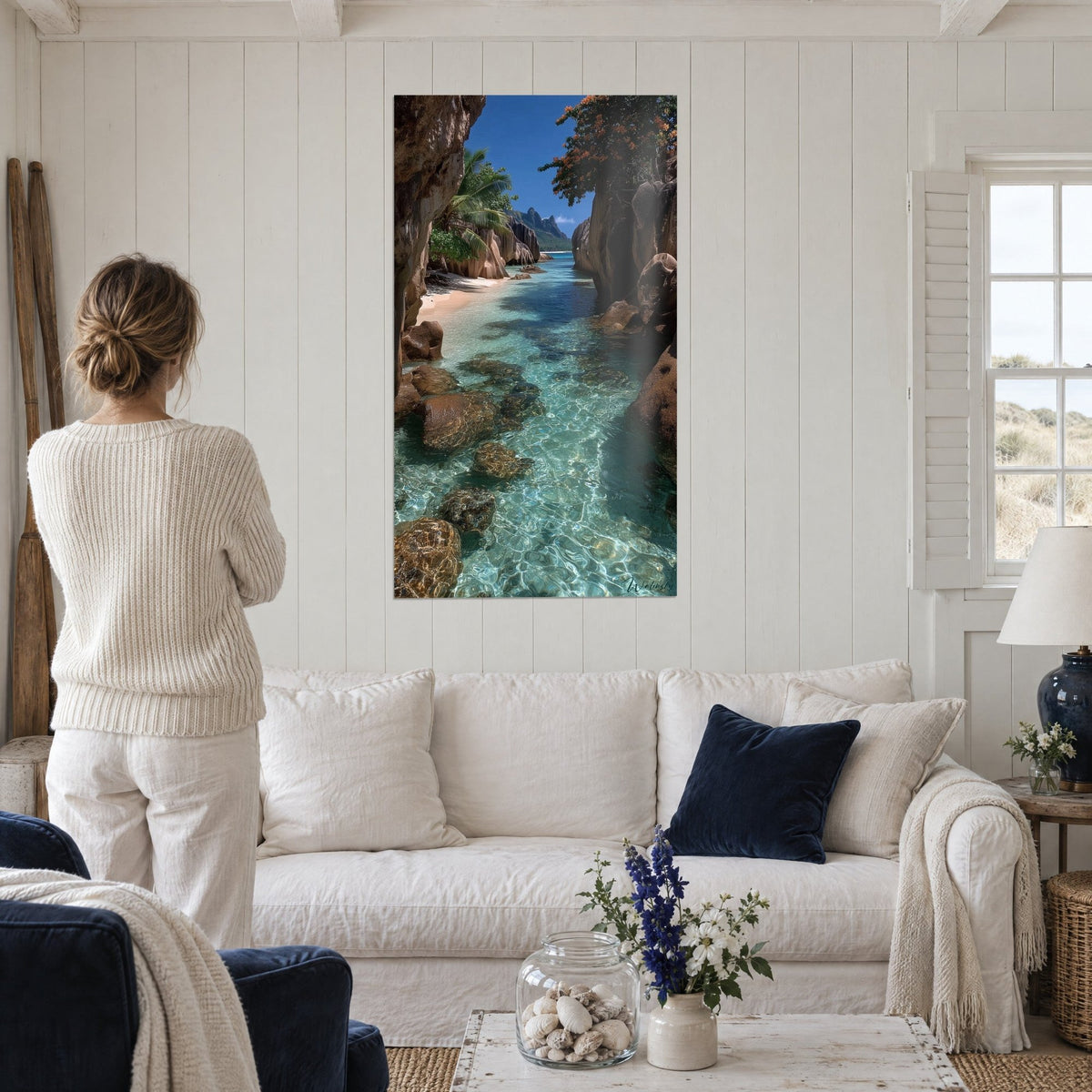 Schilderij turquoise lagune tussen okerkleurige granieten rotsen, blauwe lucht, vrouw van achteren, boven een bank in een lichte woonkamer