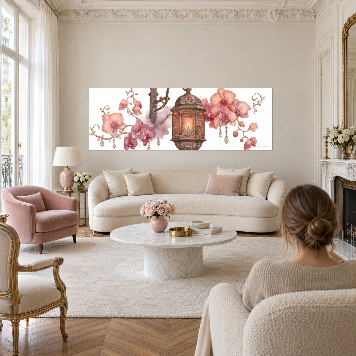 Wall art with openwork bronze lantern, amber candle and salmon-pink orchids, woman seen from behind above a sofa in a bright living room