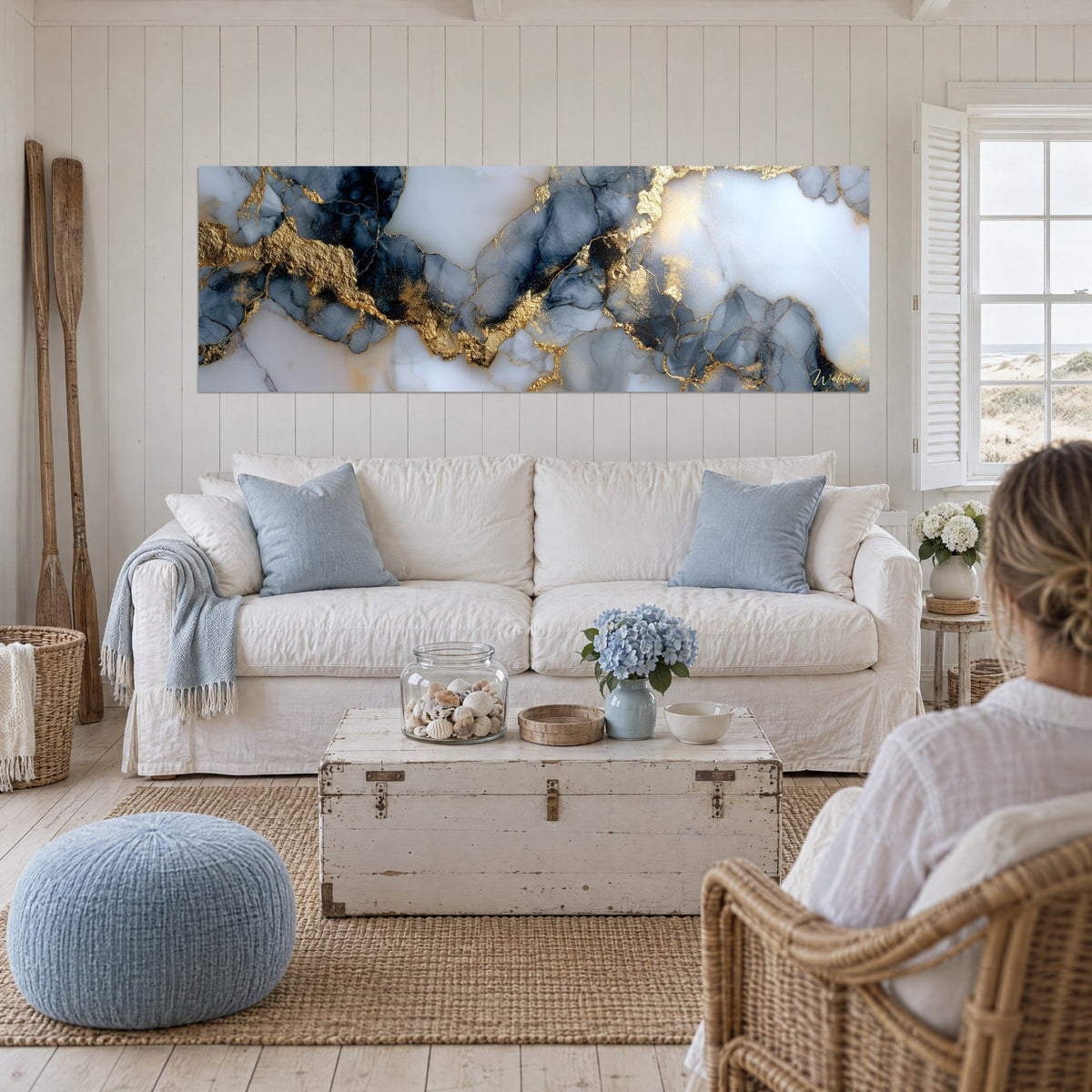Tableau marbre abstrait aux veines d'or sur fond gris bleuté, regardé de dos au-dessus d'un canapé dans un salon lumineux