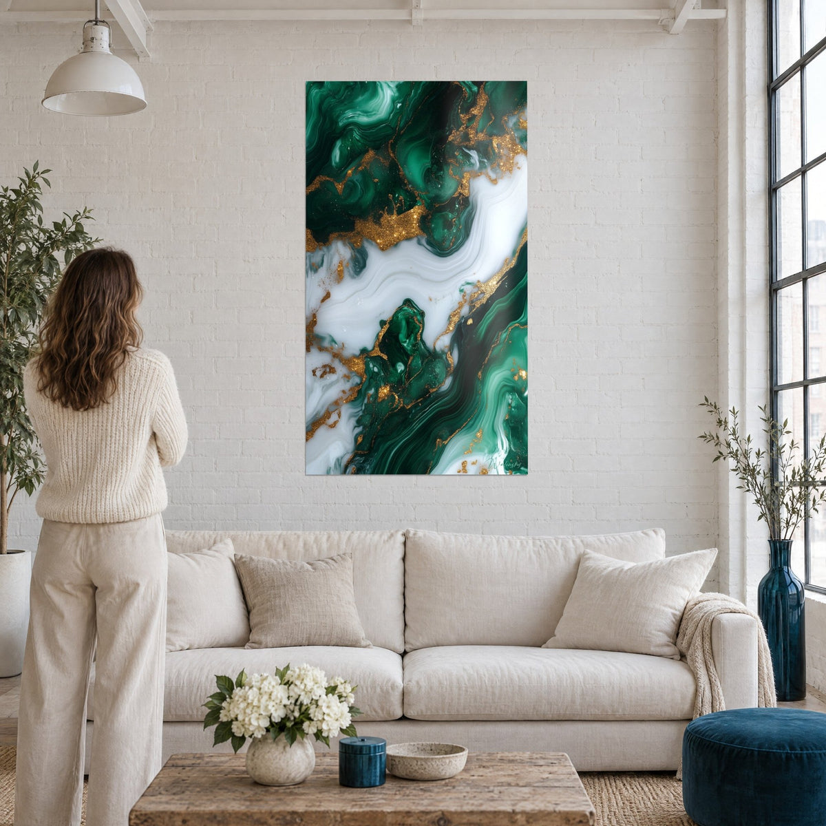 Tableau marbre fluide émeraude veiné d'or, une femme de dos le regarde au-dessus d'un canapé dans un salon lumineux
