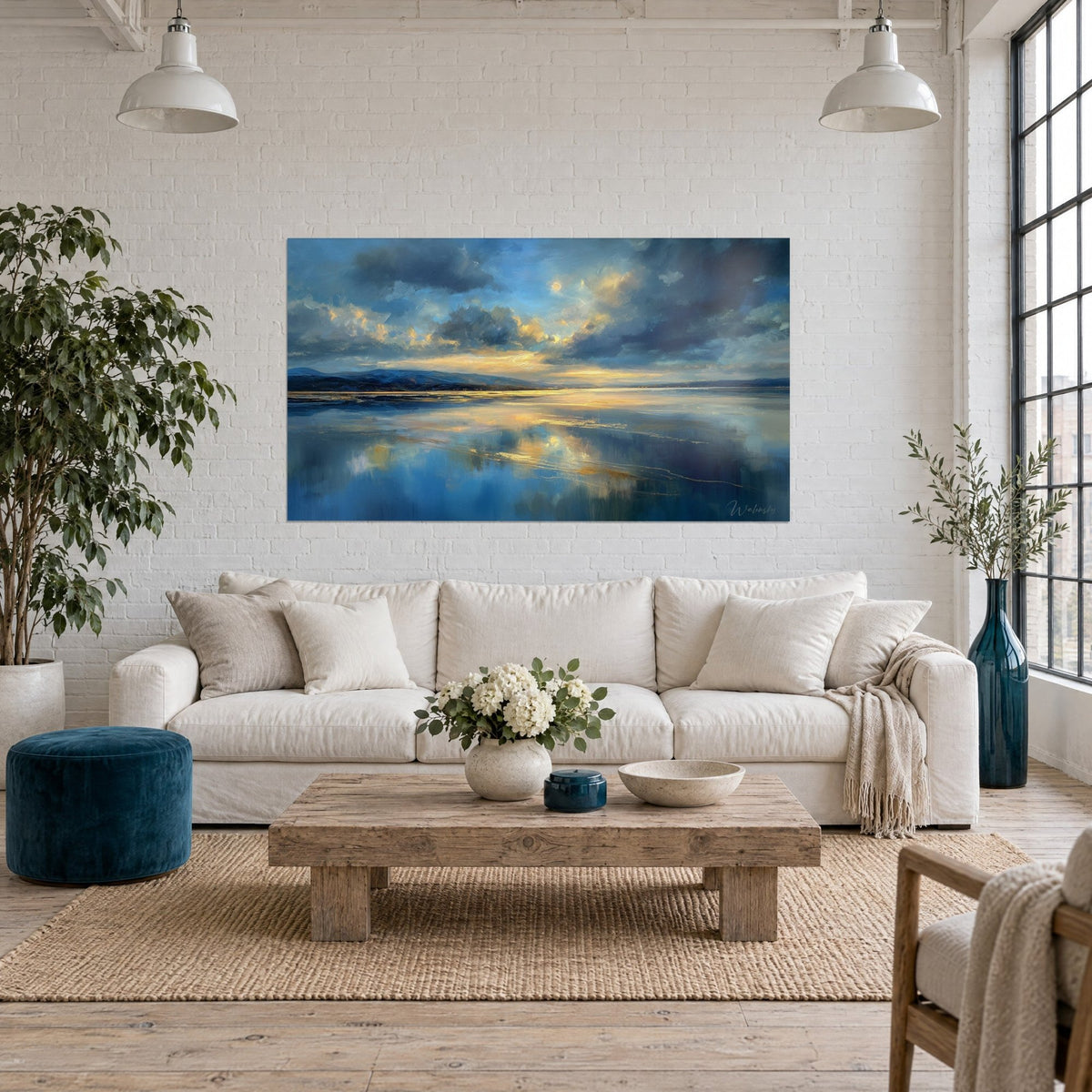 Wall art lake at dusk, midnight-blue clouds edged in gold and reflections on calm water, above a sofa in a bright living room