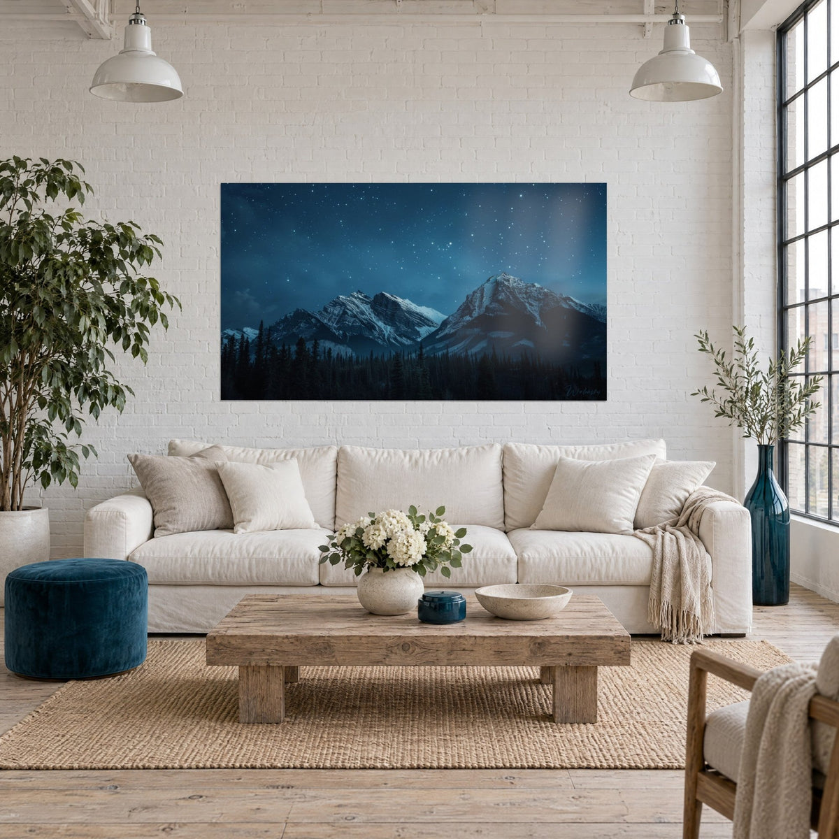 Wall art snow-capped peaks under a deep blue starry night sky, black pines at the base, hung above a sofa in a bright living room