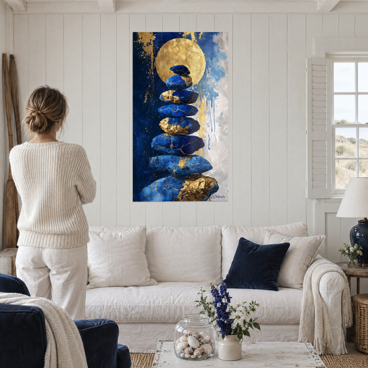 Schilderij stapel lapis lazuli keien onder een gehamerde gouden schijf, nachtblauw en goud, boven een bank in een lichte woonkamer