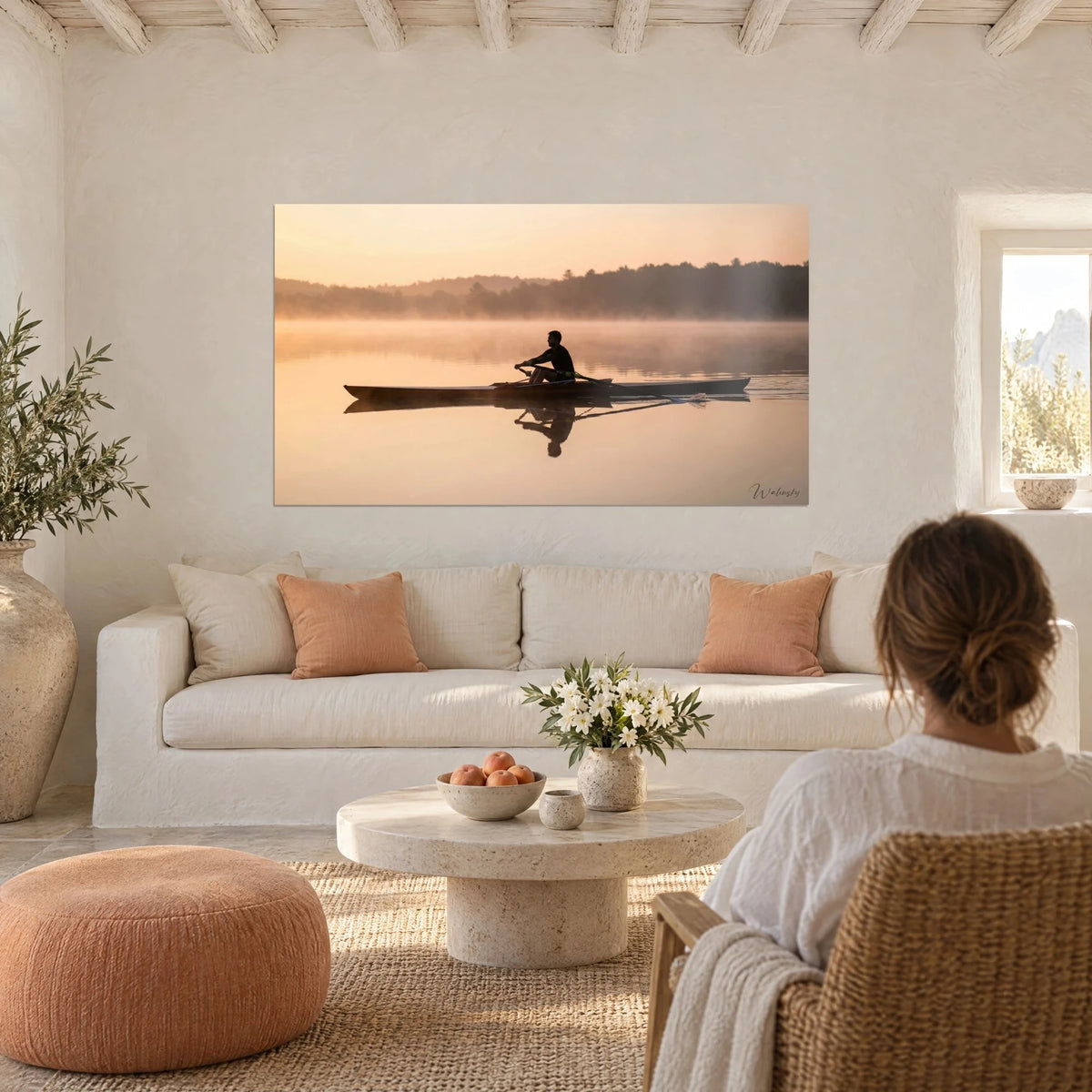 Wall art rower in silhouette on misty lake, peach sky and ochre waters, two people seen from behind above a sofa in a bright living room