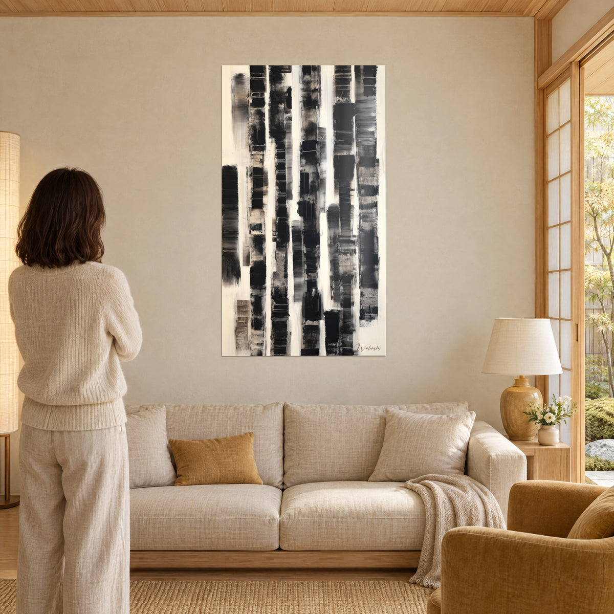Cuadro de rayas verticales negras sobre fondo crema, pinceladas estriadas; mujer de espaldas, sobre un sofá en un salón luminoso