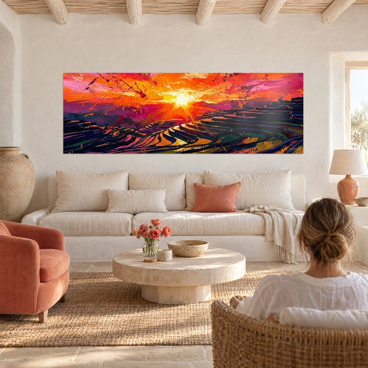 Quadro sole fiammeggiante sopra terrazze di risaie, cielo arancio e rosa vivo, donna di spalle, sopra un divano in un soggiorno luminoso