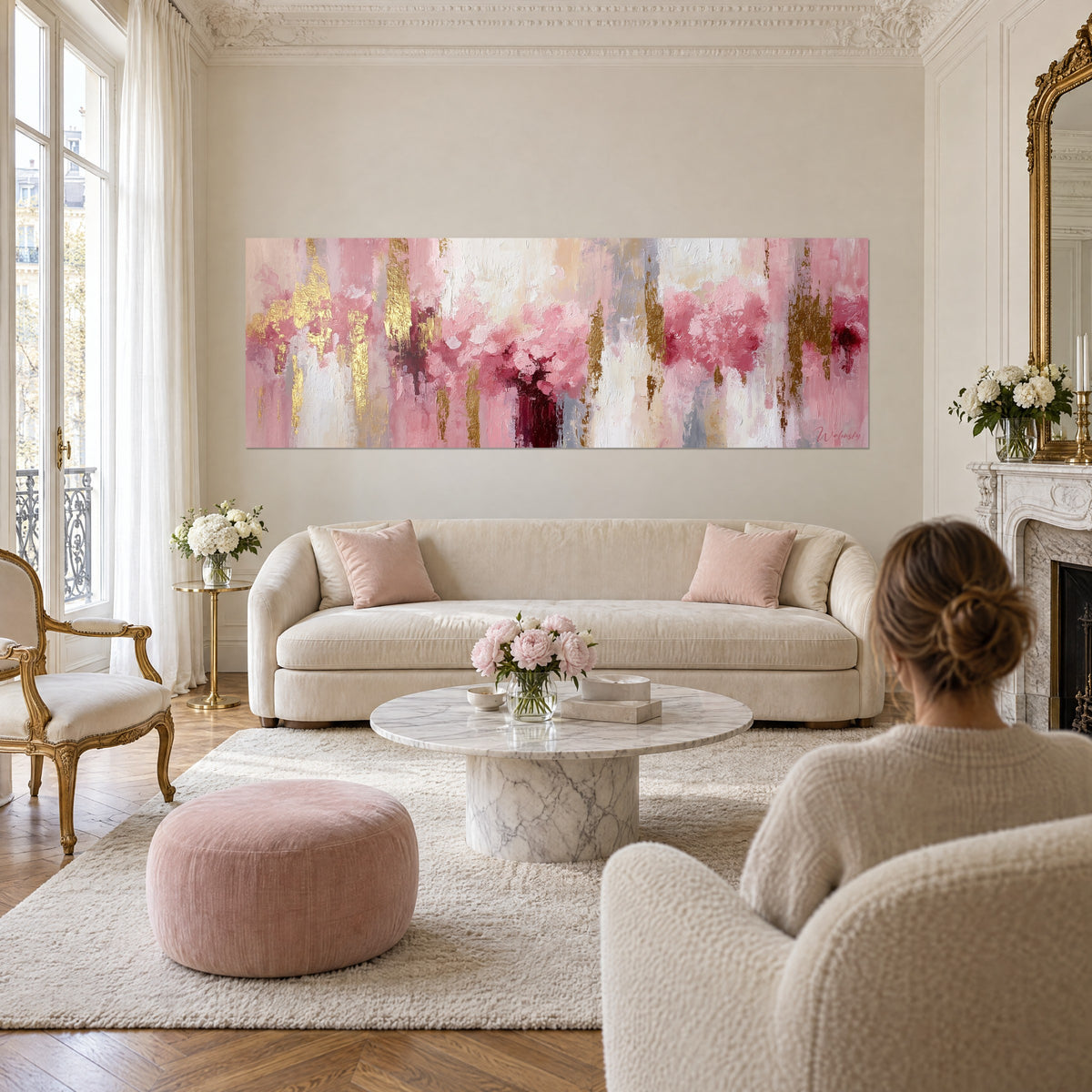 Cuadro abstracto de peonías en rosa polvoriento y pan de oro sobre fondo marfil, pareja de espaldas, sobre un sofá en un salón luminoso