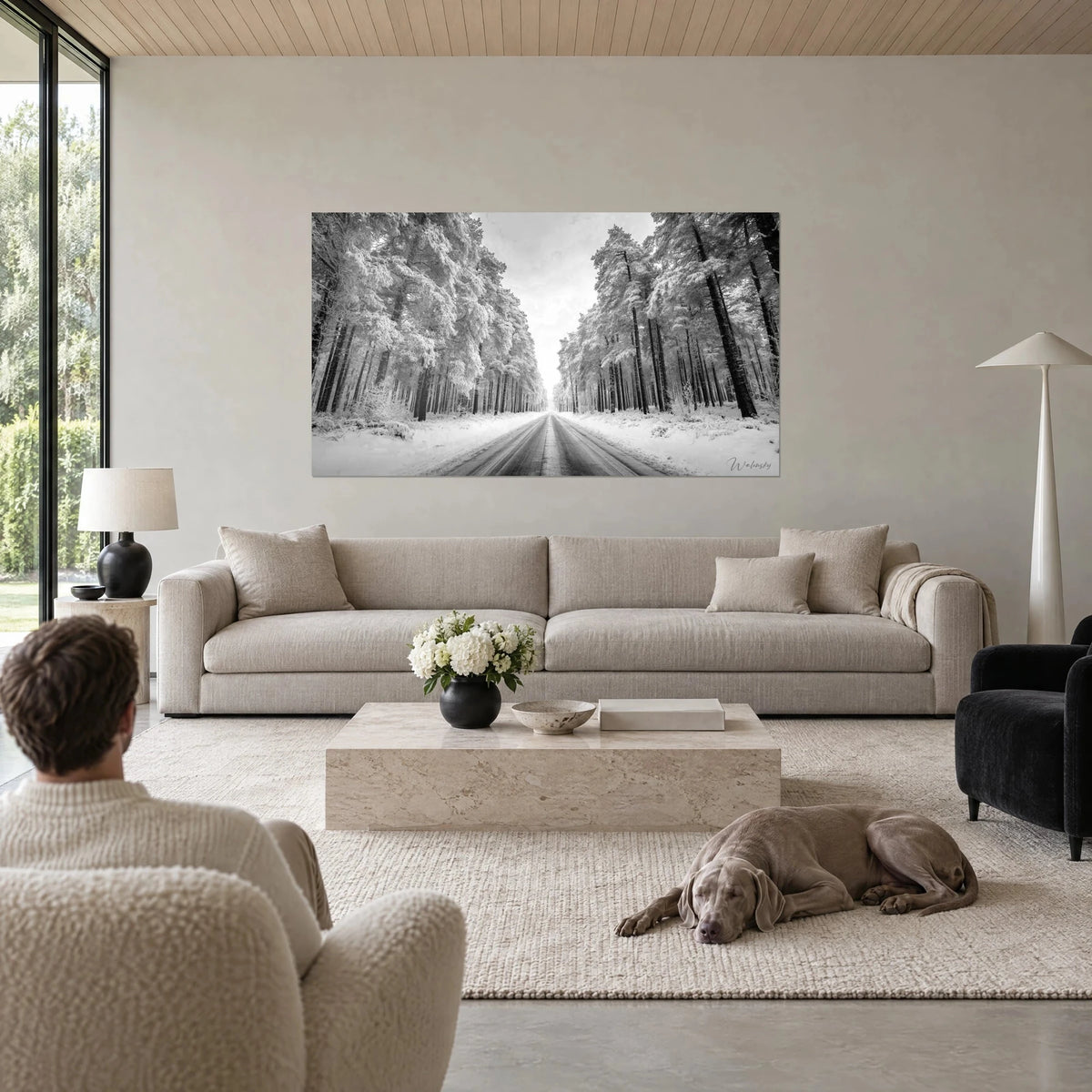 Tableau route enneigée filant entre deux murs de pins givrés, noir profond et blanc poudreux, au-dessus d'un canapé dans un salon lumineux