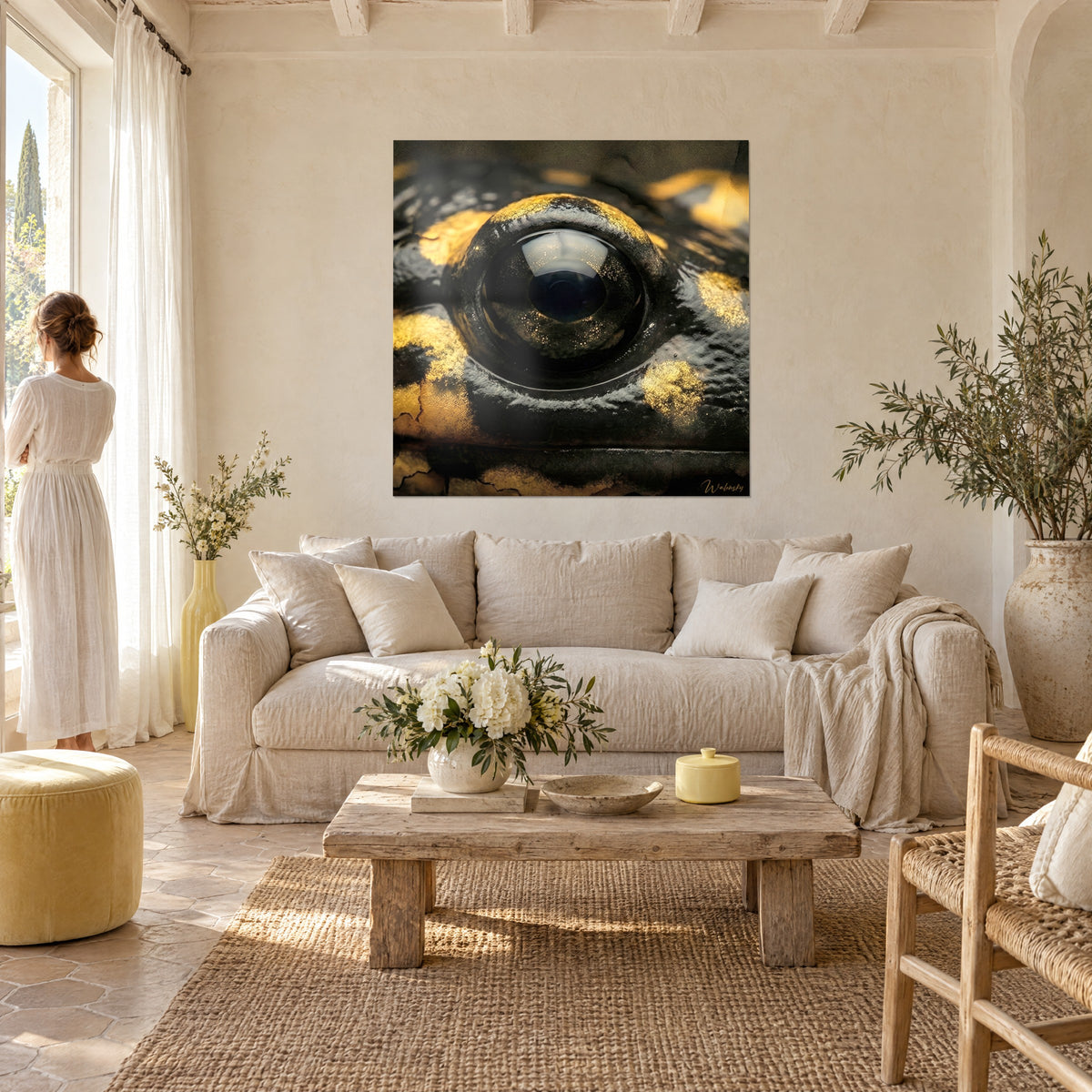 Wall art black salamander eye with a glossy pupil and golden-yellow spots, woman in a white dress, above a sofa in a bright living room