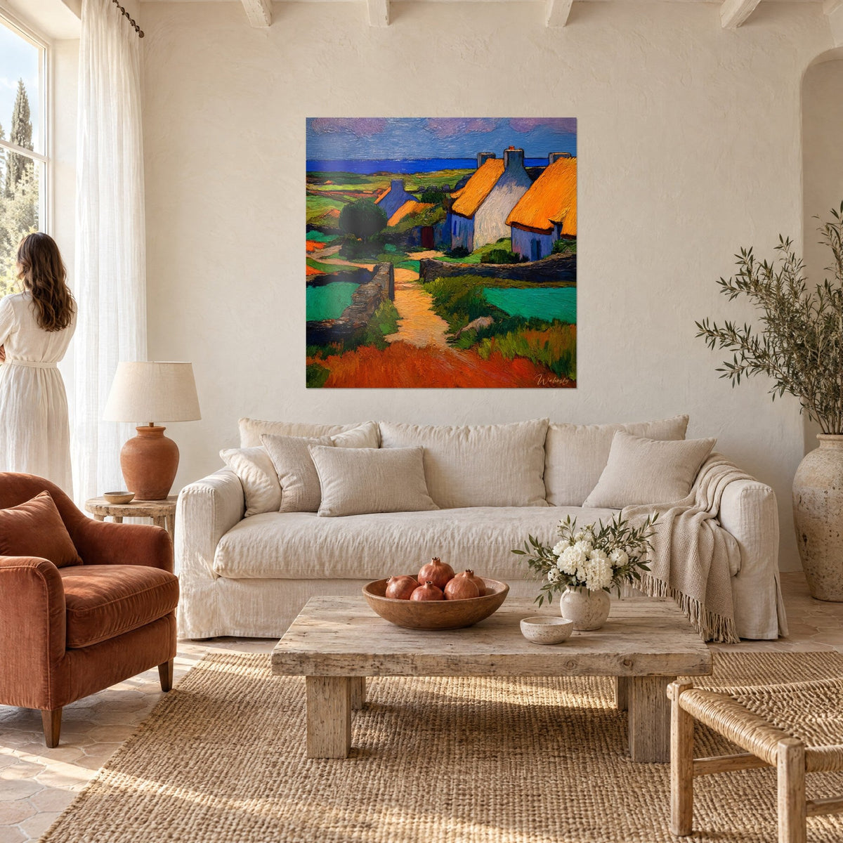 Tableau hameau breton aux toits de chaume orange et murs bleutés, mer cobalt au loin, au-dessus d'un canapé dans un salon lumineux