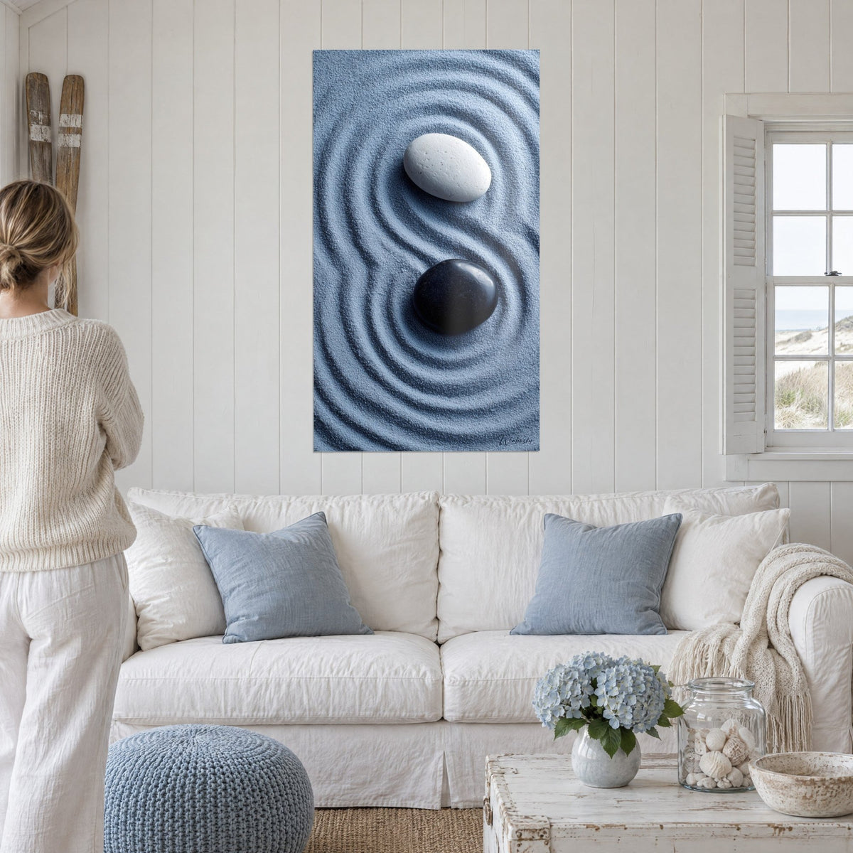 Wall art black and white zen pebbles on rippled blue sand, white wall, cream sofa, above a sofa in a bright living room