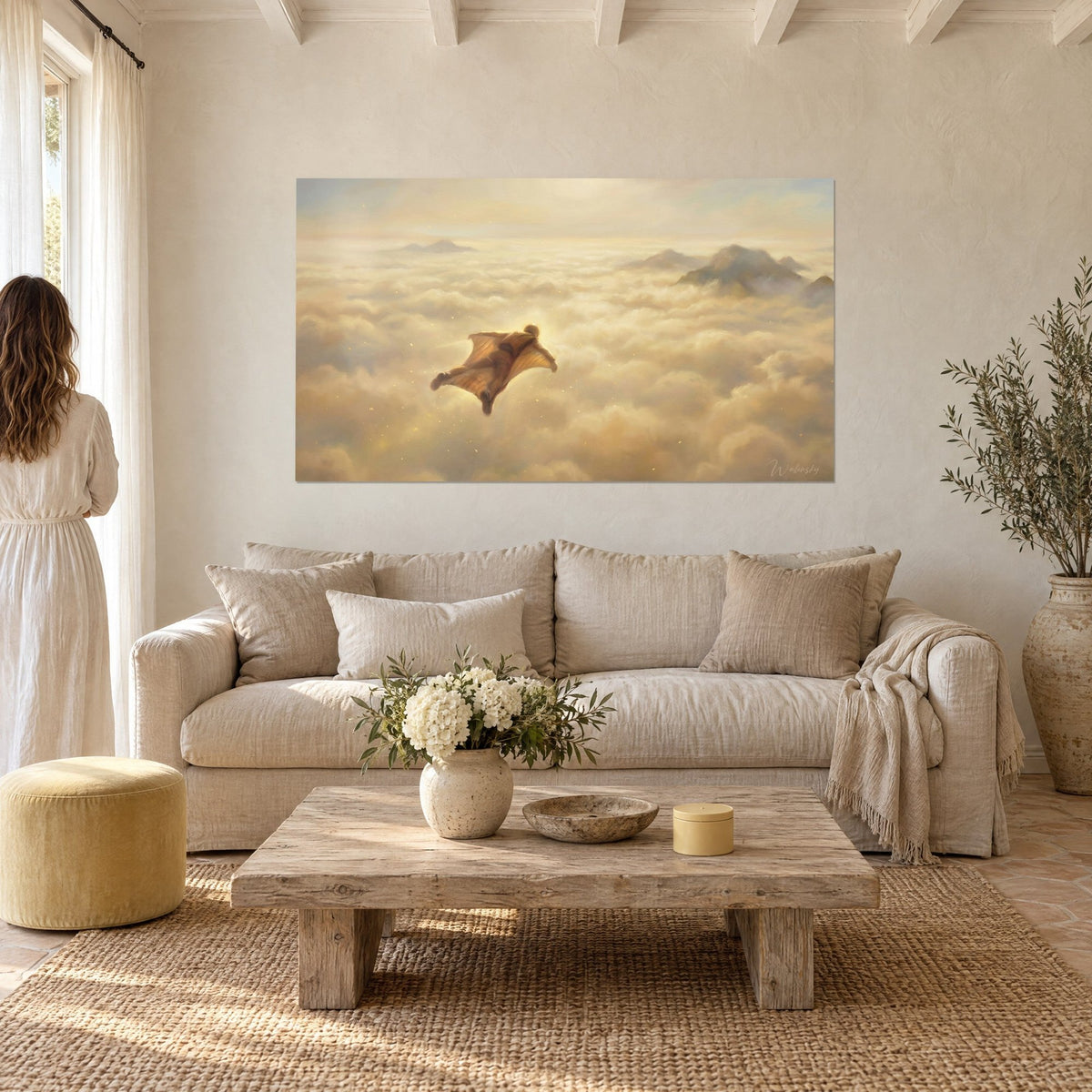 Wall art winged flyer in a wingsuit gliding over a sea of ochre and cream clouds, peaks in the distance, above a sofa in a bright living room