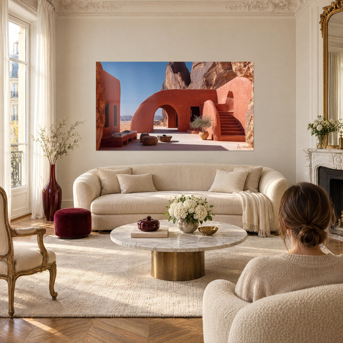 Schilderij troglodytische schuilplaats van rode gestampte aarde, blauwe lucht en okerkleurige boog, een vrouw van achteren, boven een bank in een lichte woonkamer