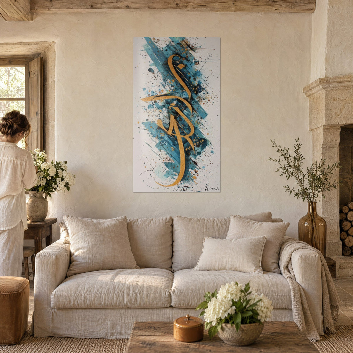 Schilderij met gouden kalligrafie over turquoise spatten, bekeken door een vrouw van achteren, boven een bank in een lichte woonkamer