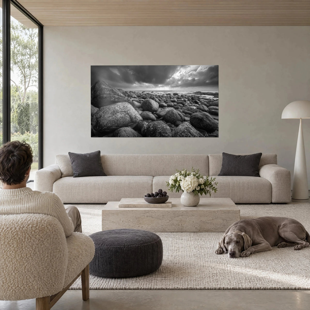 Wall art rounded pebbles beneath a stormy sky, black and white, lichen and a clear horizon, above a sofa in a bright living room