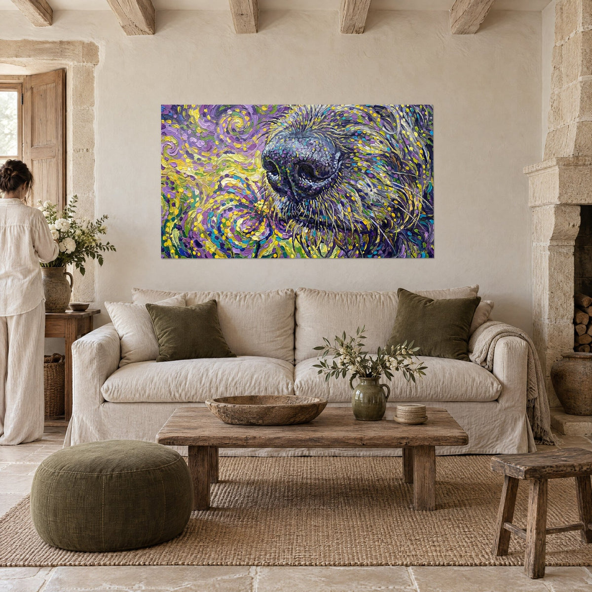 Schilderij van de snuit van een windhond met violette en gele penseelstreken, vooraan een vrouw van achteren, boven een bank in een lichte woonkamer