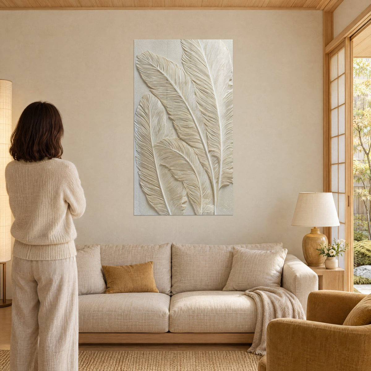 Quadro con piume scolpite in rilievo beige e avorio, barbe finemente incise, sopra un divano in un soggiorno luminoso