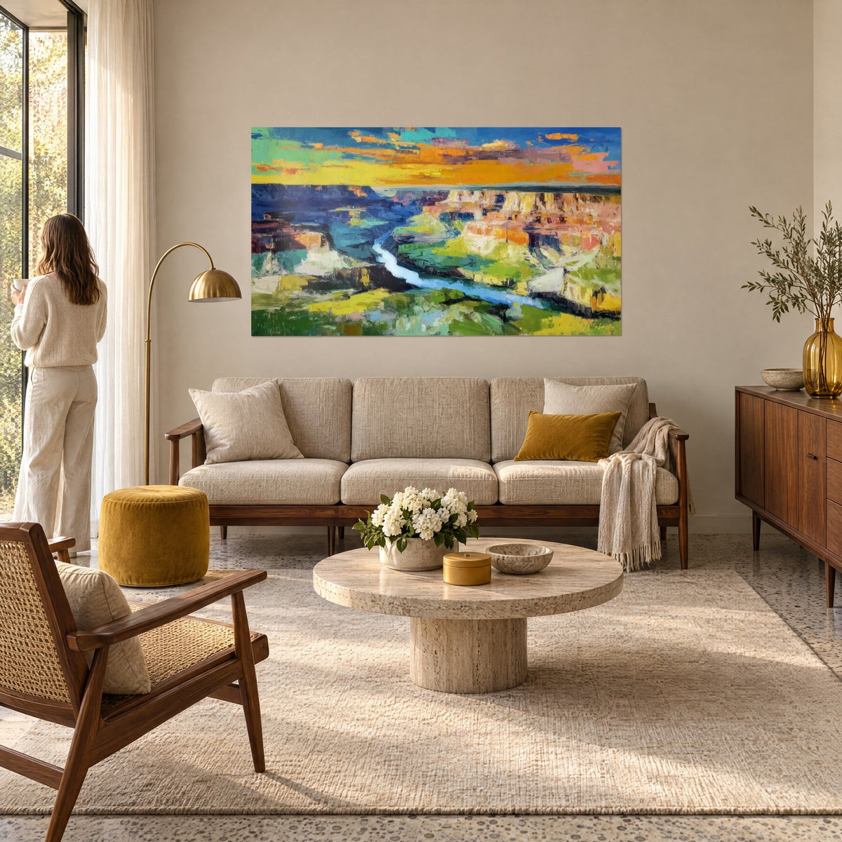 Tableau gorge profonde au ciel jaune orangé, rivière bleu clair entre falaises ocre, femme de dos, au-dessus d'un canapé dans un salon lumineux