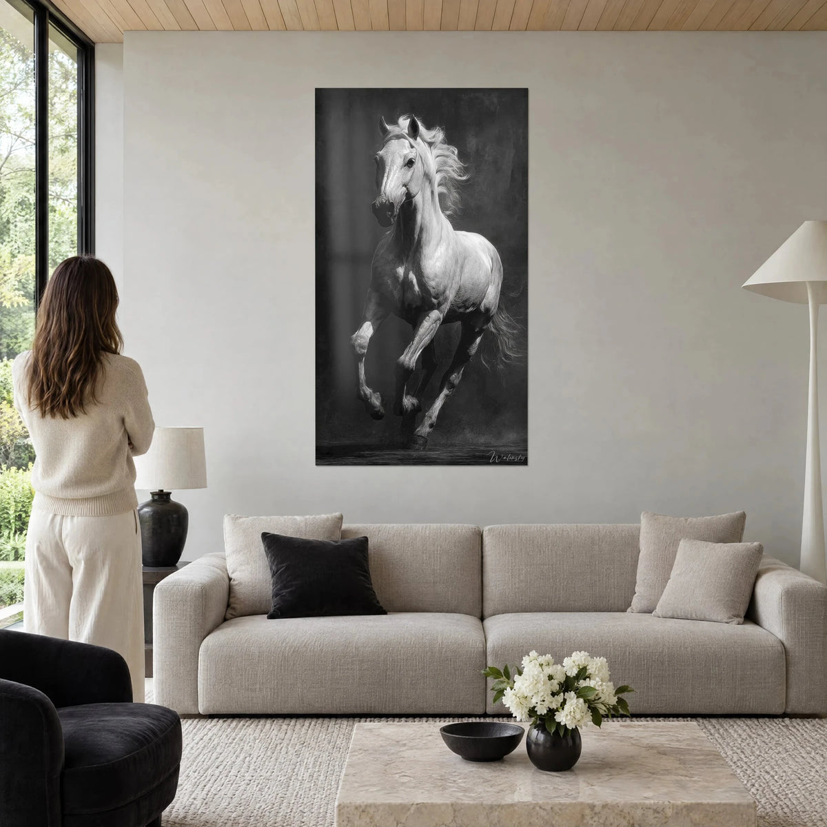 Wall art white horse galloping, swirling mane on charcoal black background, woman from behind, above a sofa in a bright living room