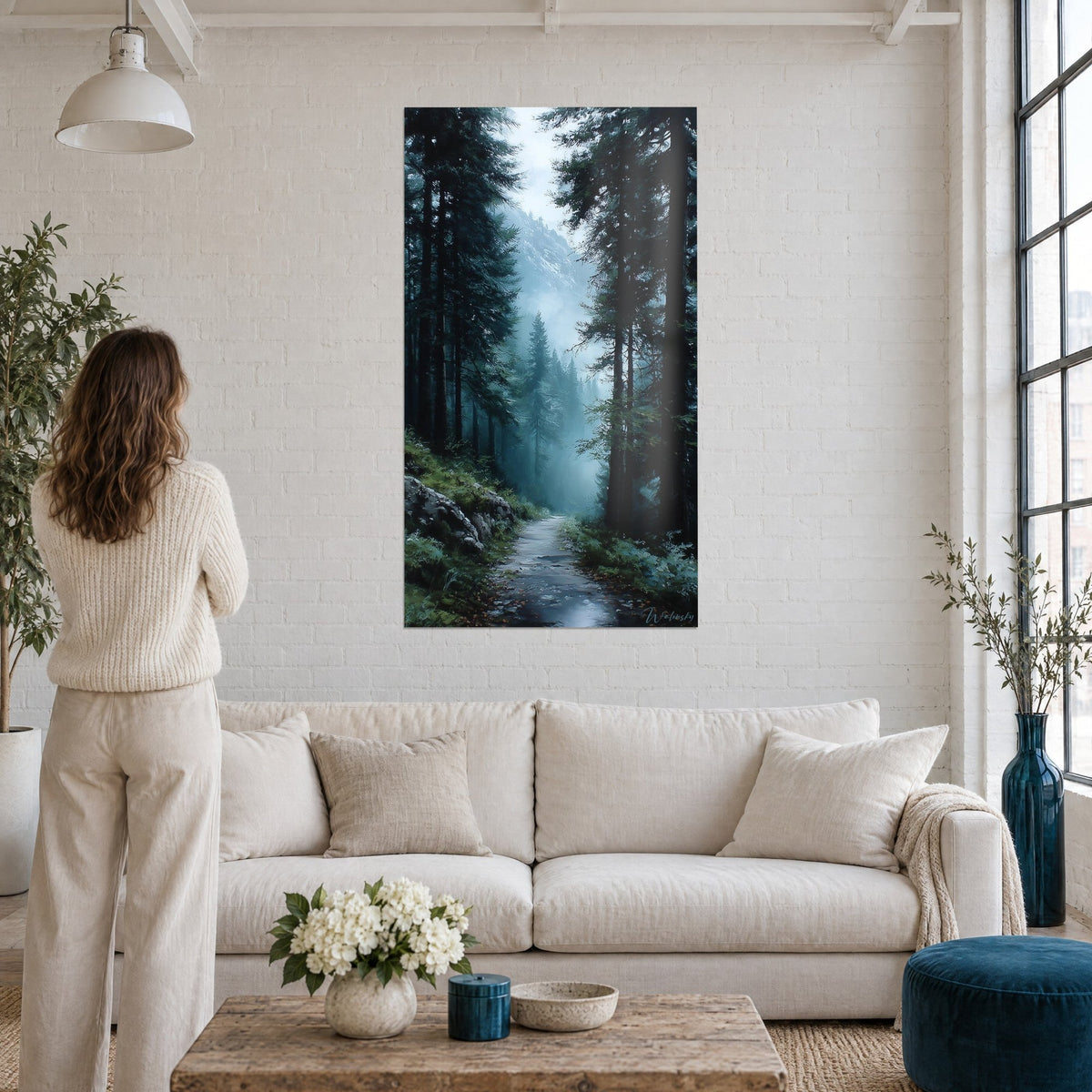 Wall art forest path in the mist, dark green fir trees and pale blue veil, above a sofa in a bright living room