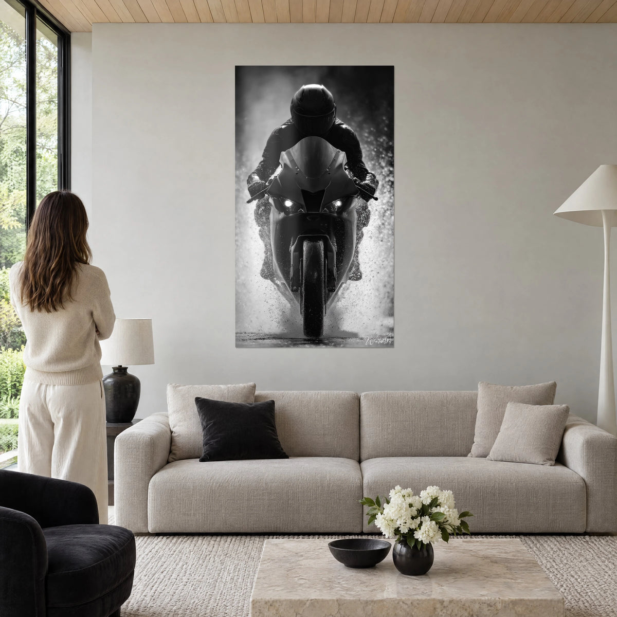 Wall art of a sport motorbike charging straight at the viewer, black helmet and white sprays of water, woman seen from behind above a sofa in a bright living room