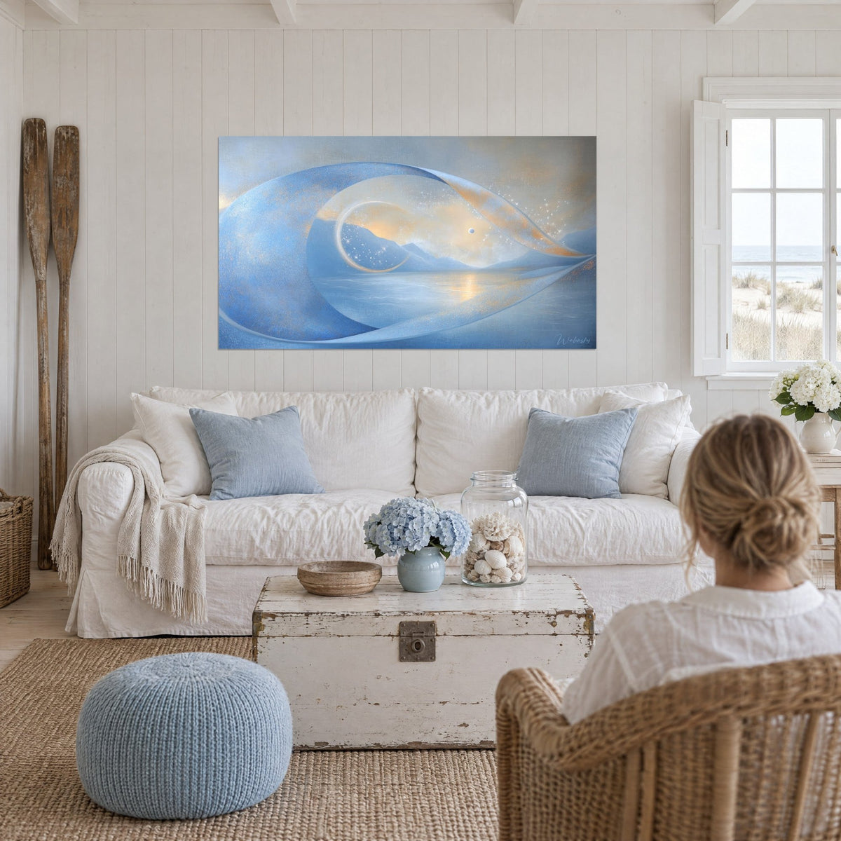 Tableau ruban d'onde bleu pervenche et dorés sur un lac embrumé, vu par une femme de dos, au-dessus d'un canapé dans un salon lumineux