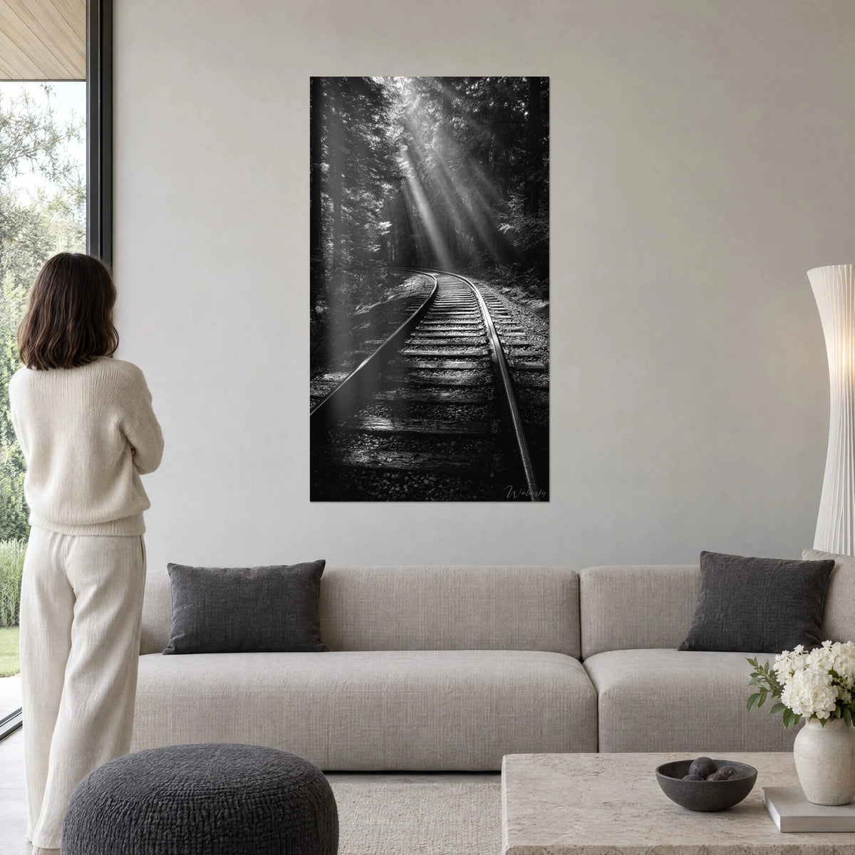 Cuadro vía férrea sinuosa bajo rayos de luz plateados, bosque en blanco y negro, encima de un sofá en un salón luminoso