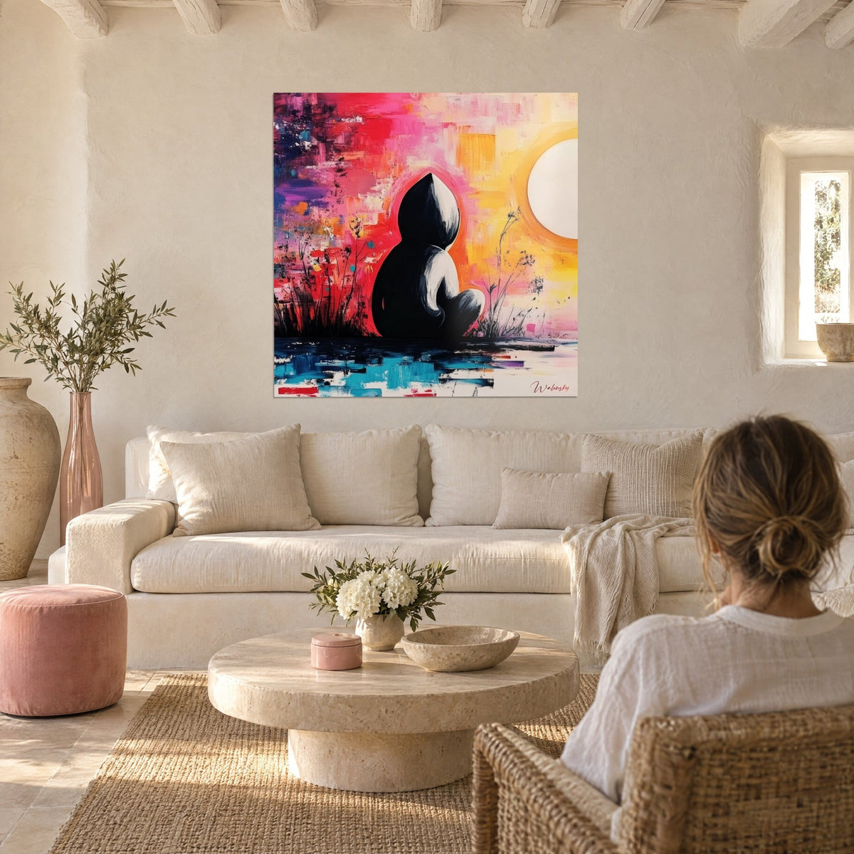 Wall art black silhouette seated facing a white sun, pink background, red and yellow, above a sofa in a bright living room