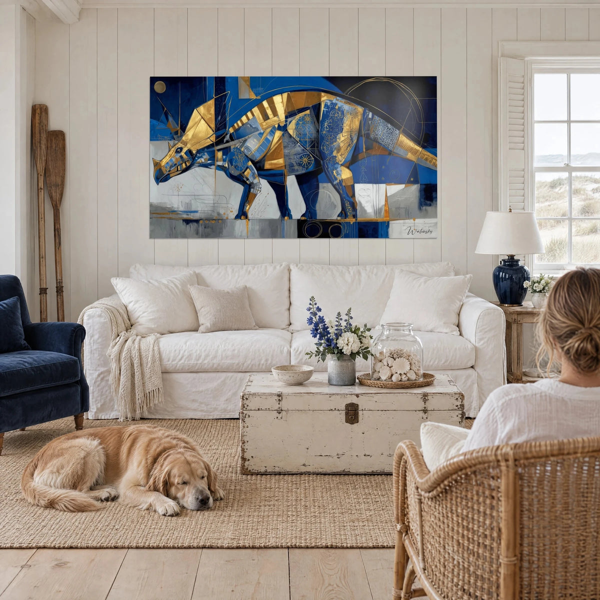 Tableau tricératops géométrique bleu cobalt et or, corne dorée, facettes éclatées, au-dessus d'un canapé dans un salon lumineux
