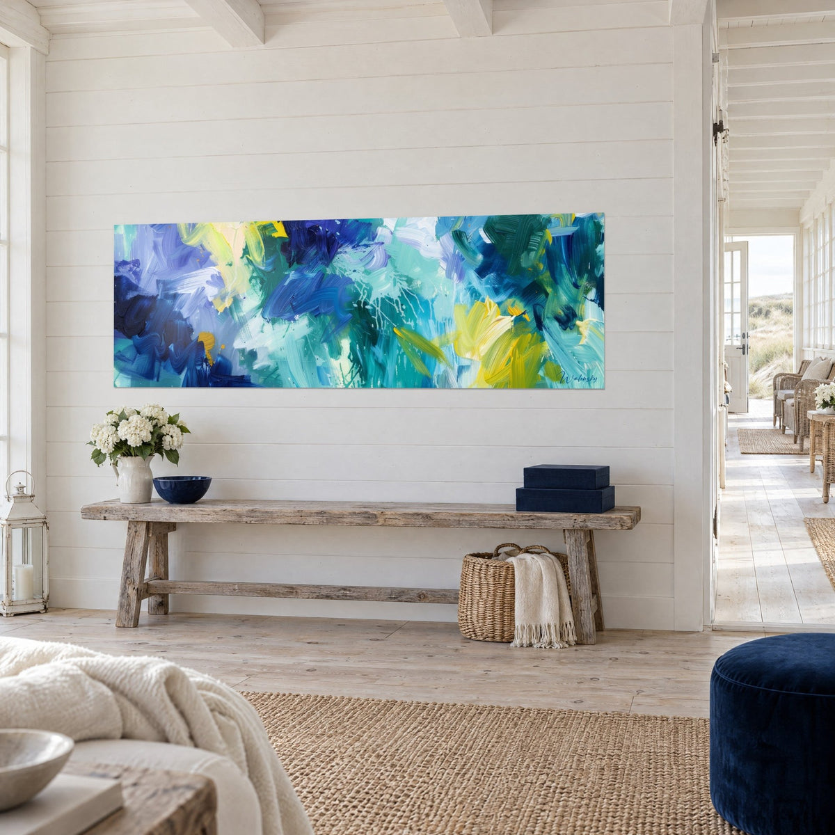 Tableau toile panoramique de touches turquoise et vert profond, éclats jaunes sur mur blanc lambrissé, vue de trois-quarts, console rustique et bouquet blanc