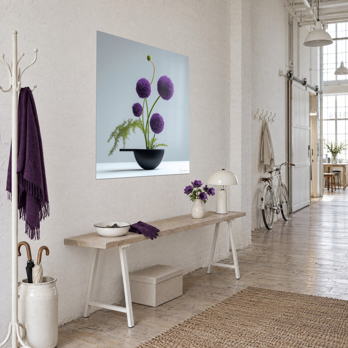 Gemälde Strauß aus purpurfarbenen Zierlauch auf grünen Stielen, schwarze Schale und perlgrauer Hintergrund, hängend in einem Künstler-Loft mit weißer Ziegelwand
