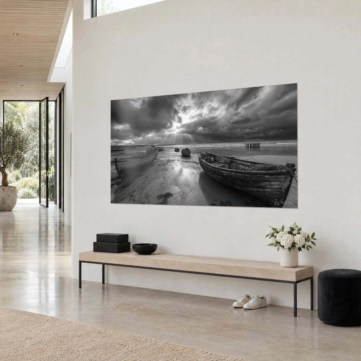 Tableau coque de bois usée sur la grève mouillée, nuages anthracite et lumière argentée, accroché sur un mur beige près d'un banc