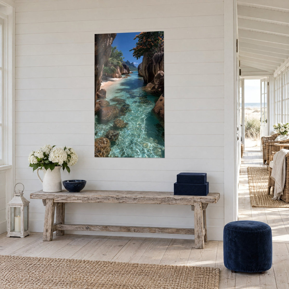 Schilderij tropische baai met kristalhelder smaragdgroen water, bruine rotsen en oranje gebladerte, aan de witte muur van een strandhuis