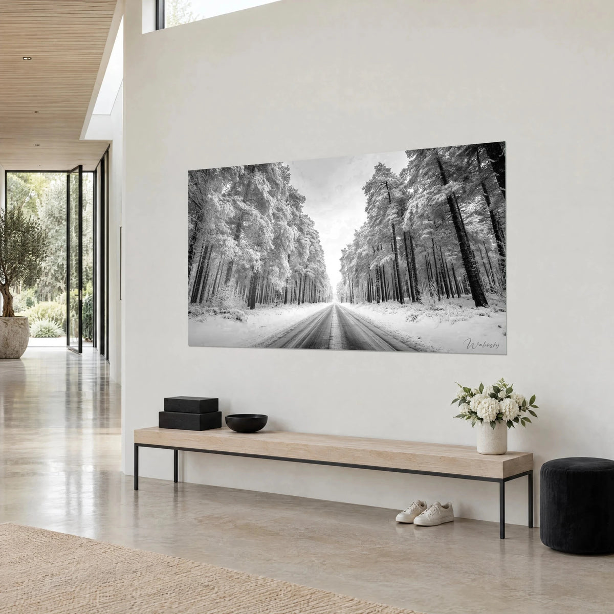 Tableau chemin d'hiver bordé de sapins chargés de neige, ciel gris perle et troncs noirs, accroché dans une maison d'architecte