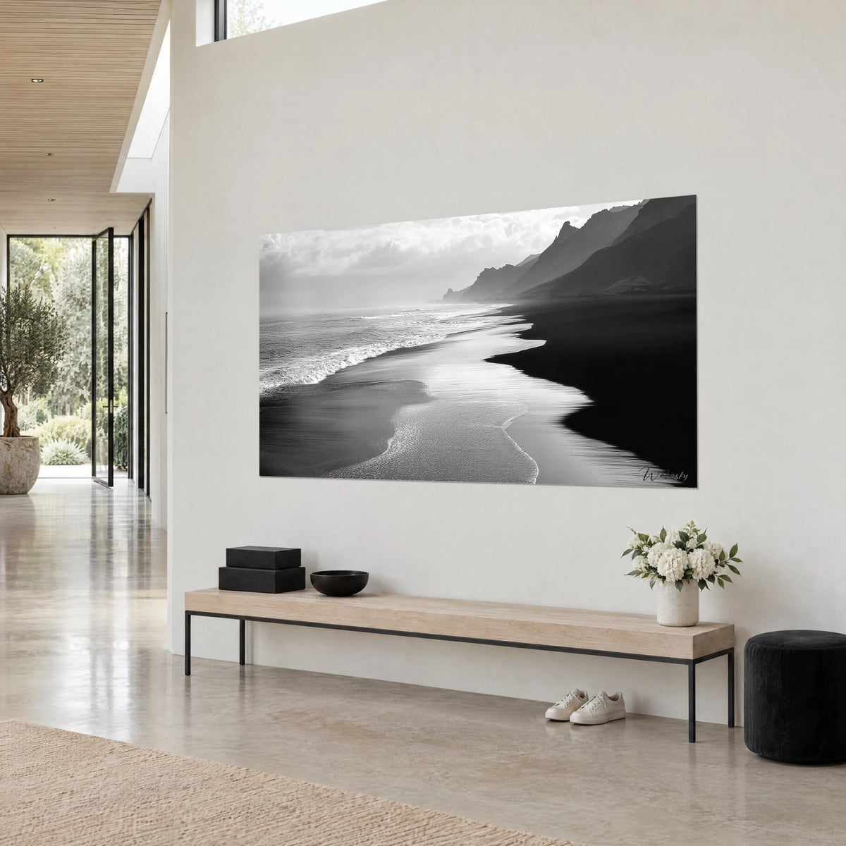 Wall art wild shoreline where a silvery wave snakes across black sand, cloudy grey sky, on a beige wall of an architect-designed house