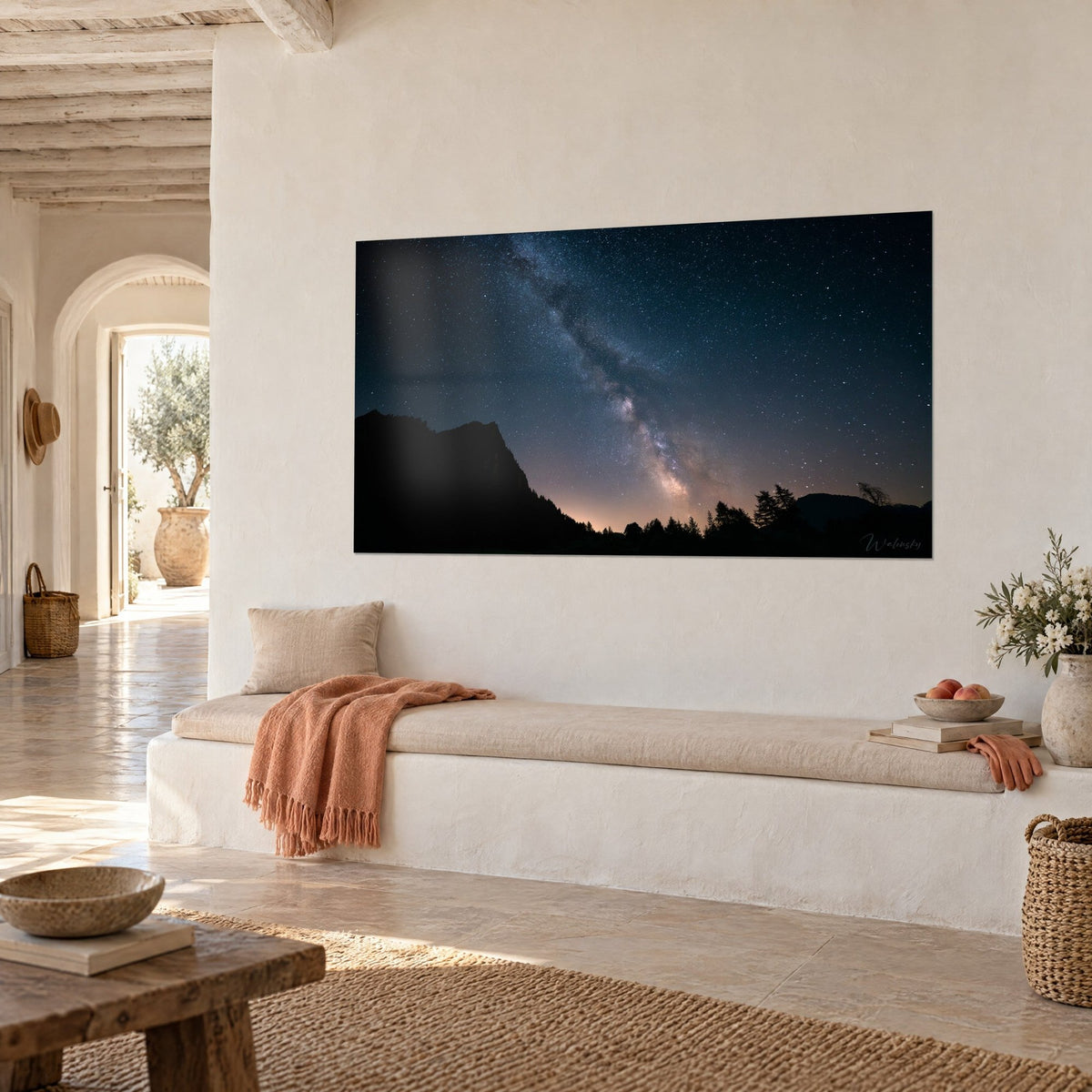 Tableau galaxie scintillante bleu marine et lueur orangée à l'horizon, accroché sur un mur blanc, banquette en pierre claire