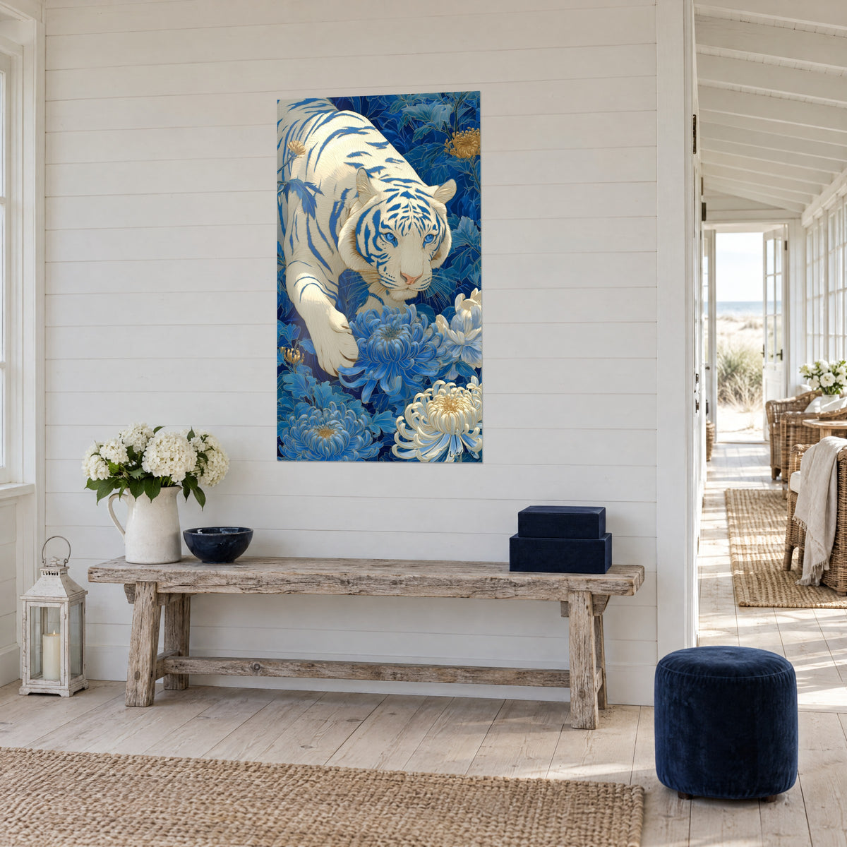 Quadro di un felino color avorio striato di blu, con la zampa sollevata tra fiori indaco e crema, vista a tre quarti accanto a una consolle in legno chiaro