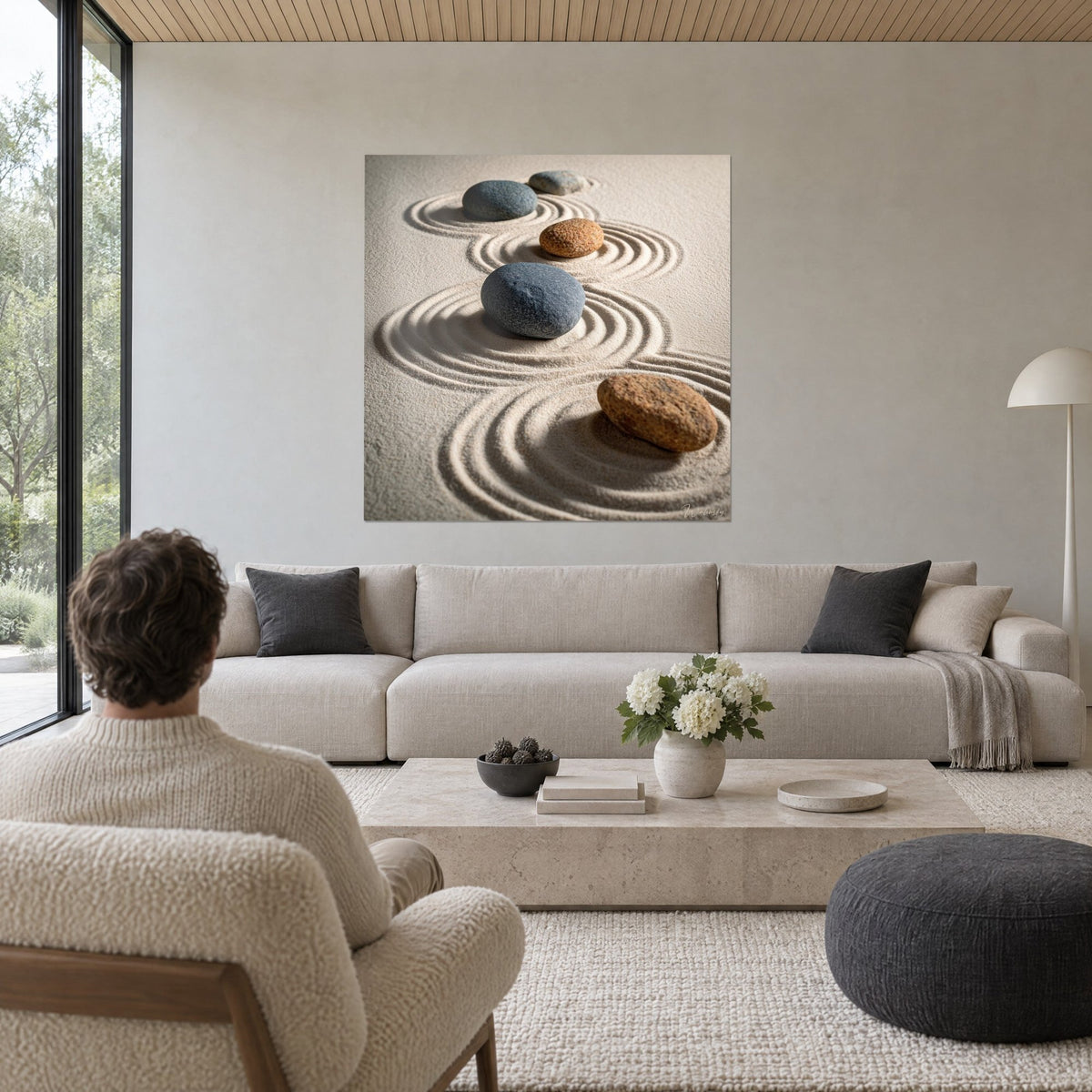 Tableau galets zen aux reflets bleu ardoise et ocre sur sable ratissé, au-dessus d'un canapé dans un salon lumineux