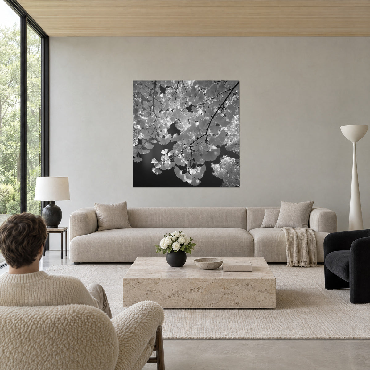 Schilderij met waaiervormig ginkgobladerwerk, parelgrijs en diep zwart, fijne takken, boven een bank in een lichte woonkamer