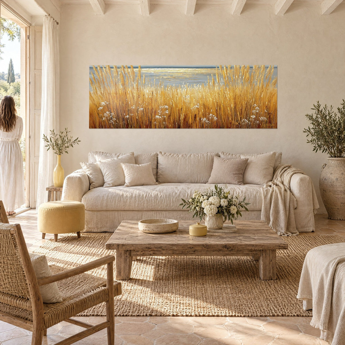 Quadro erbe dorate ondeggianti davanti a un mare grigio, fiori bianchi, ocra e blu acciaio, sopra un divano in un soggiorno luminoso