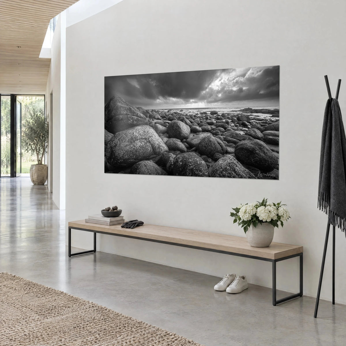 Wall art granite rock beach in black and white, dark clouds and a brightened sky, hung on a white wall of an architect's house