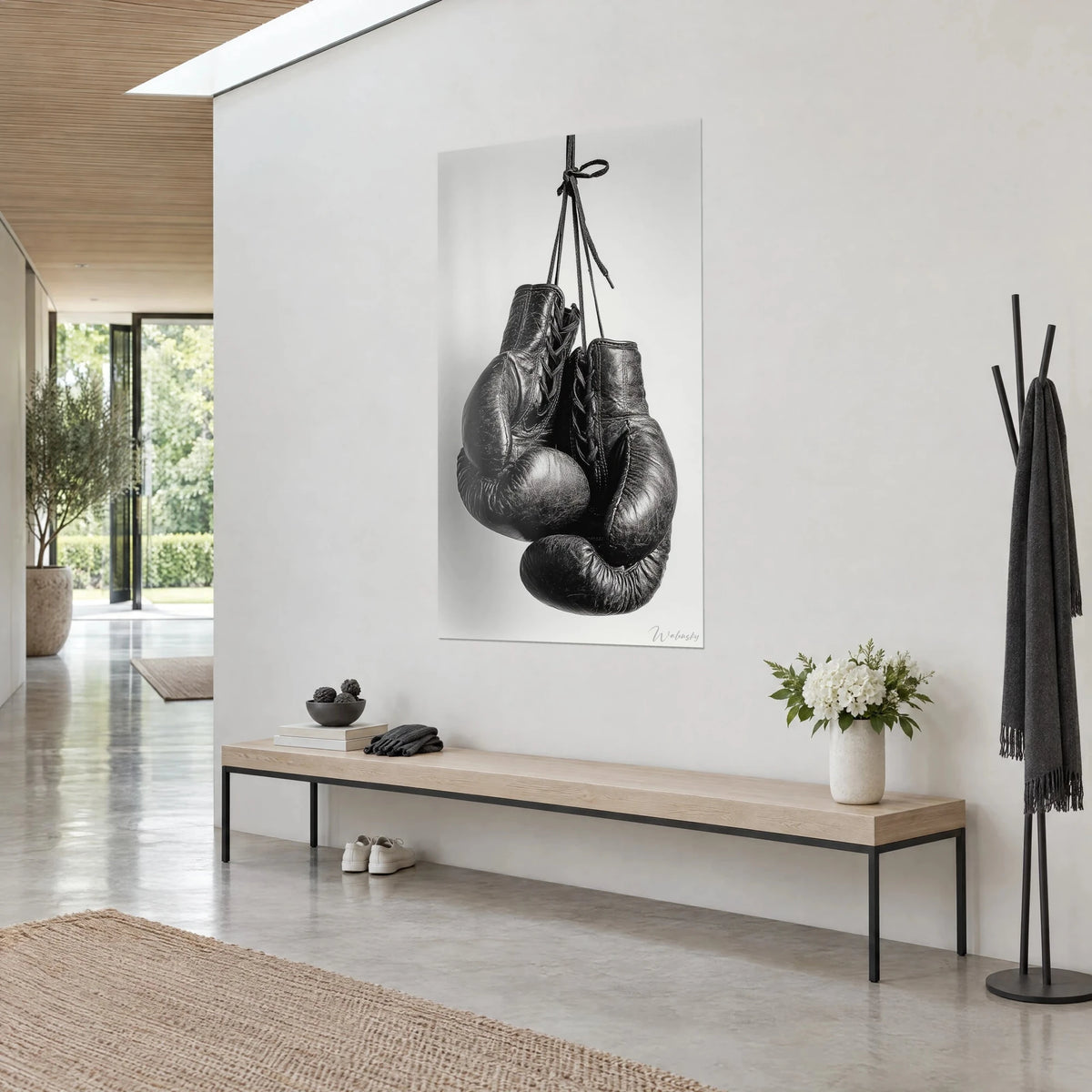 Tableau paire de mitaines de ring pendues par leurs lacets, cuir noir patiné et fond gris clair, banc en bois dans l'entrée
