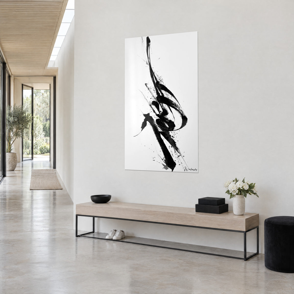 Wall art with black ink spiral, splashes on off-white background, hung above a light wood console in a hallway