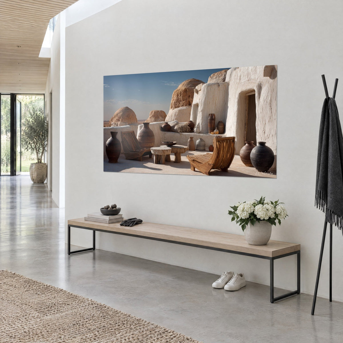 Wall art cream-toned cave architecture under an azure sky, light wooden chairs and dark jars, on the wall of a concrete-plaster entrance