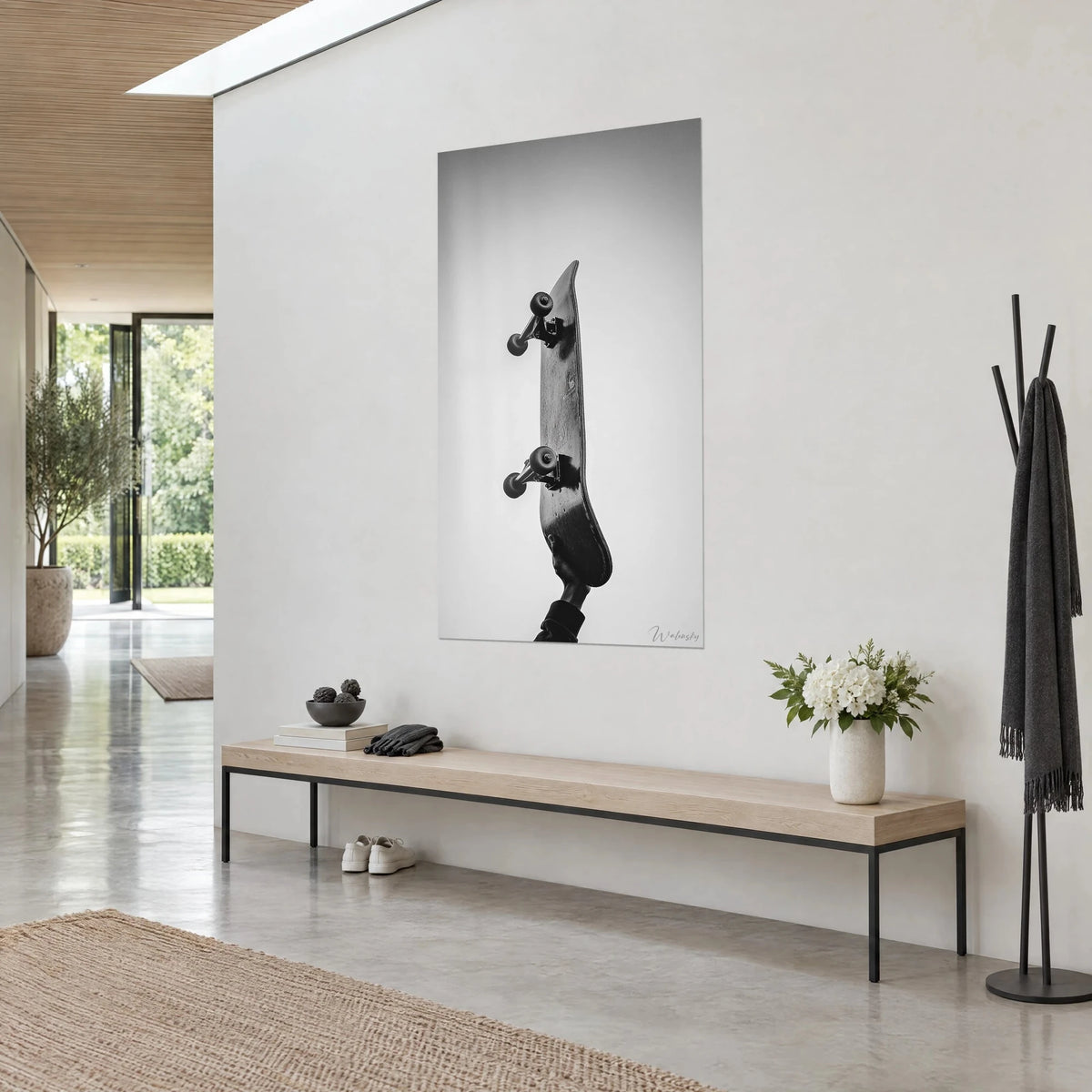 Quadro tavola da skate sollevata a braccio teso, nero profondo su fondo grigio perla, appesa vicino a una panca in legno chiaro