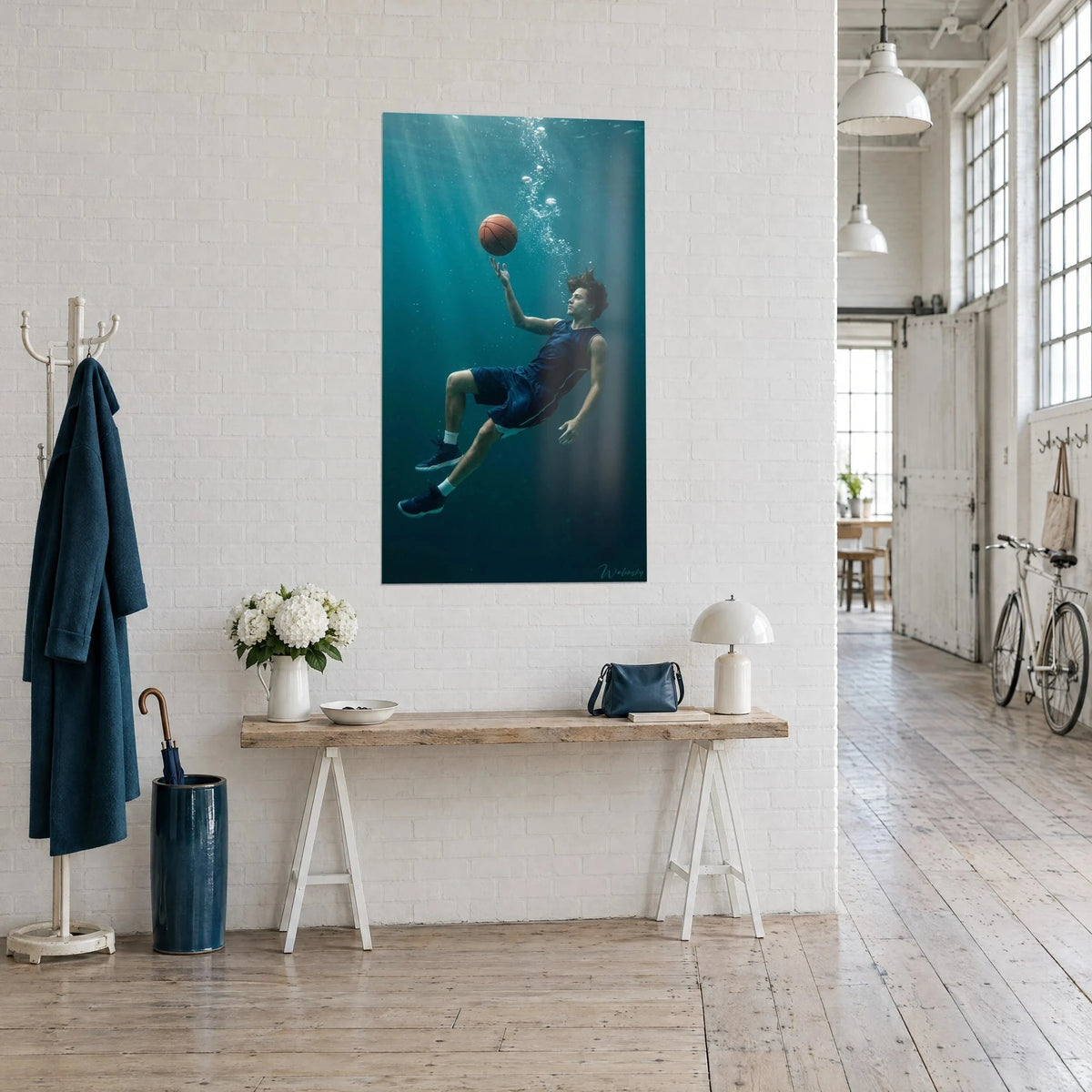 Sportief schilderij in gewichtloosheid, uitgestrekte arm richting een oranje bal in blauw-groene lichtstralen, aan een witte muur van een kunstenaarsloft