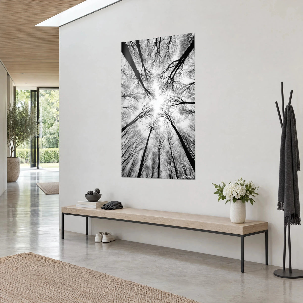 Wall art forest seen from below, fine black branches against milky white sky, hung above a bench in light wood and grey