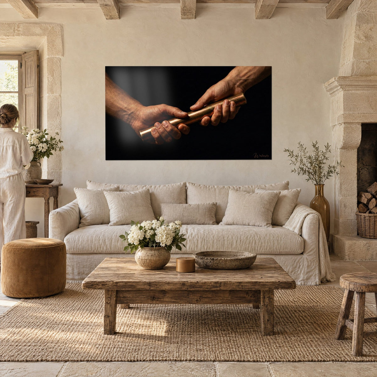 Tableau passage de témoin en cuivre entre deux mains burinées, fond noir, bronze et ocre, au-dessus d'un canapé dans un salon lumineux