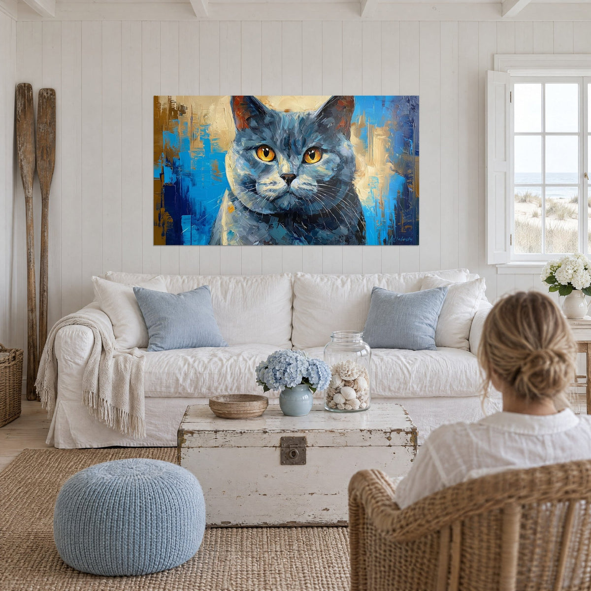 Cuadro de gato cartujo de pelaje gris azulado y ojos dorados, fondo turquesa y ocre, encima de un sofá en un salón luminoso